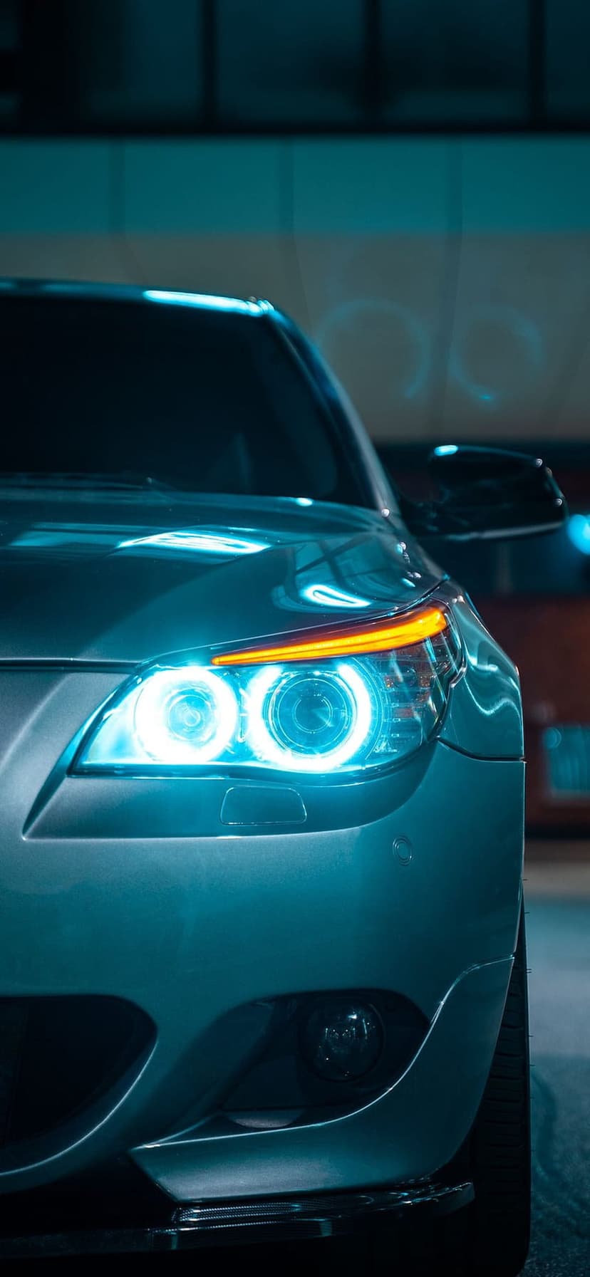 Neon blue circular car headlights glow beside an amber turn signal on a sleek grey metallic automotive exterior.