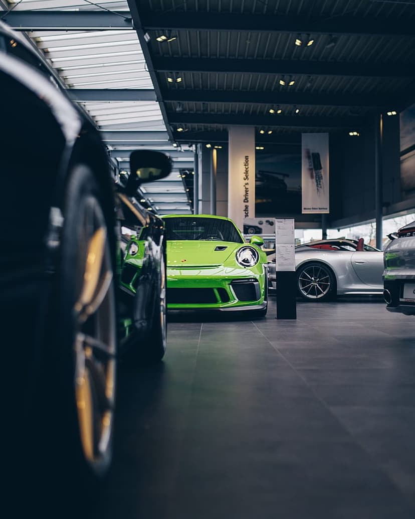 Lime green Porsche GT3RS and silver convertible parked on a glossy showroom floor with overhead studio lighting.