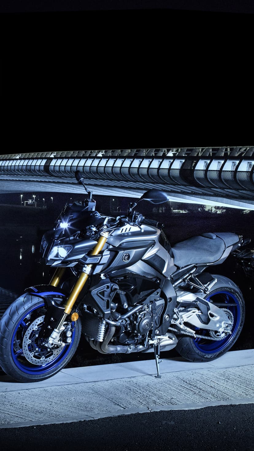 Yamaha MT-10 motorcycle with blue wheels parked beneath a modern bridge structure with glowing city lights.