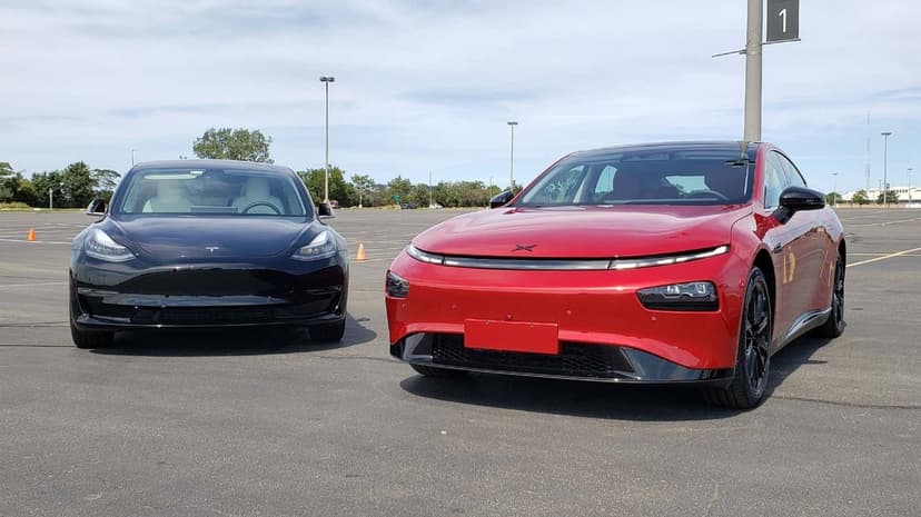 Red Xpeng P7 and black Tesla electric cars parked on a wide asphalt lot under a bright, sunny blue sky.