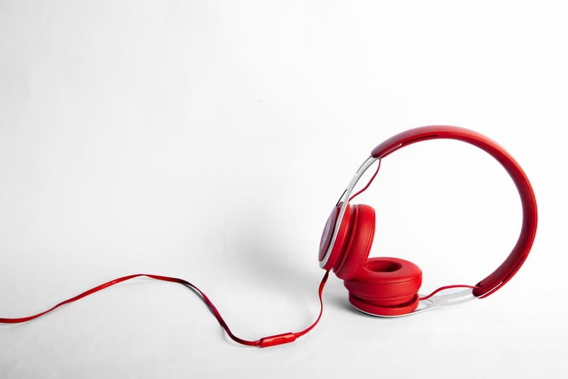 Red over-ear headphones with a coiled wire on a white surface, presented as a vertical smartphone background.