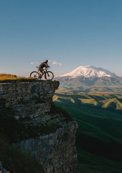 Cyclist on Cliff Edge with Snow-Capped Mountain