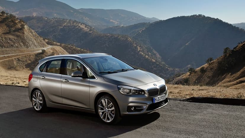 Silver BMW 2 Series Active Tourer parked on an asphalt mountain road overlooking a vast sunlit valley.
