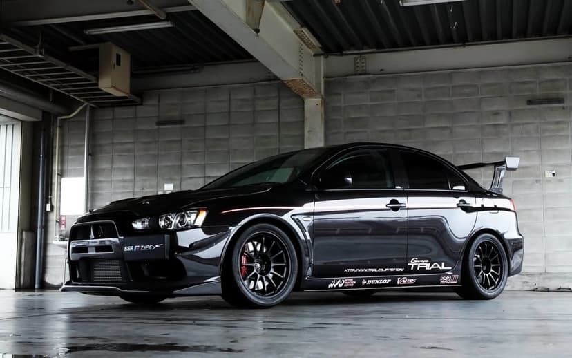 Black Mitsubishi Lancer Evolution X with a large wing parked in a concrete industrial garage under dim light.