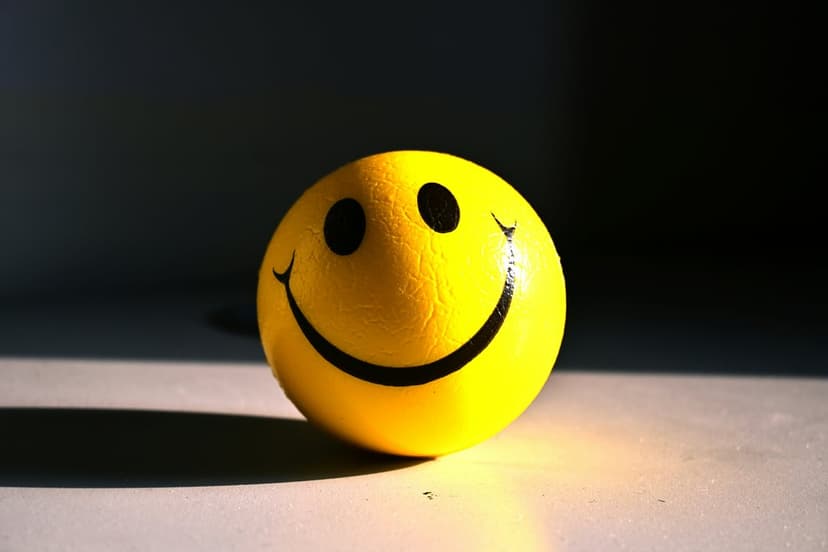 Yellow smiley face stress ball illuminated by sharp sunlight against a black background with heavy shadows.