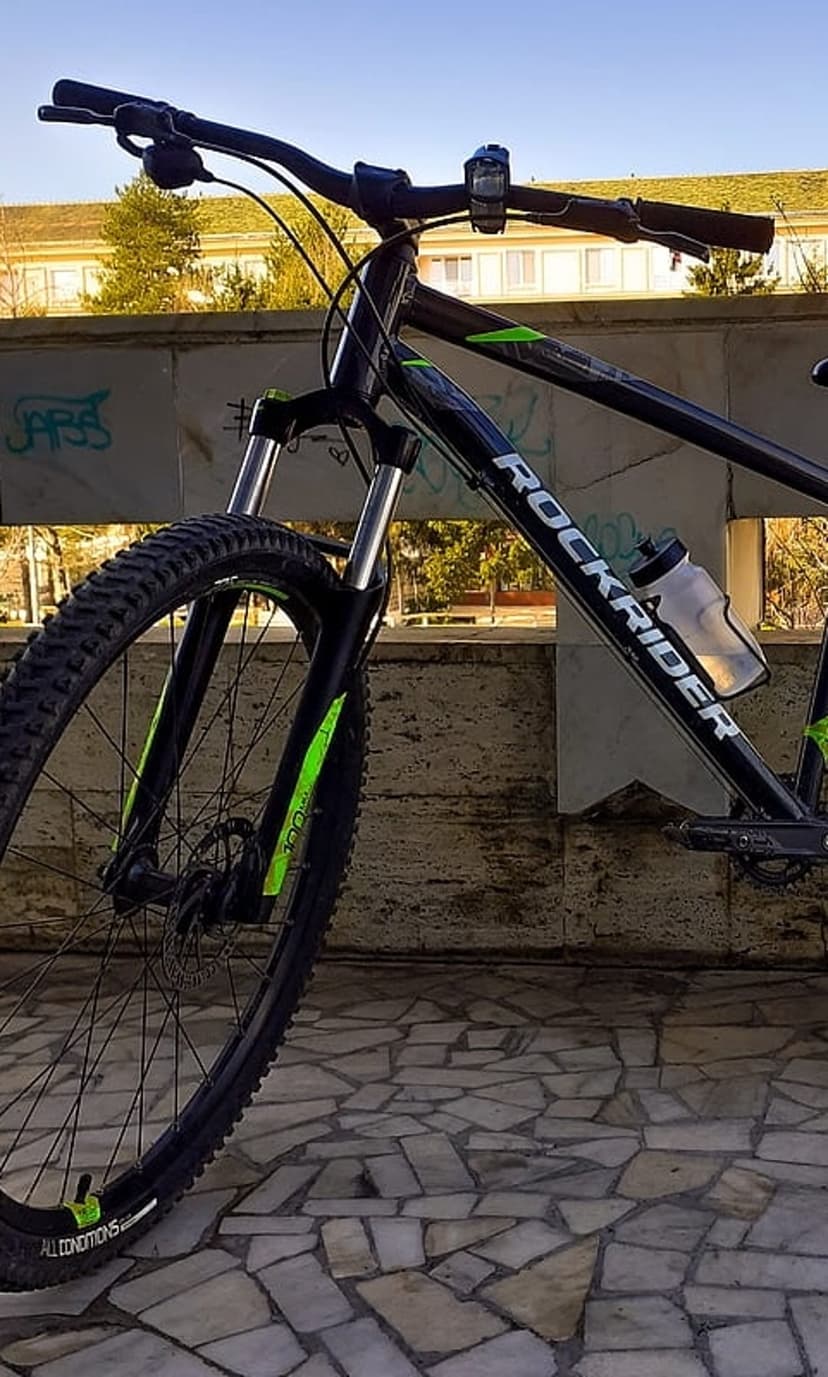 Black Rockrider mountain bike with green suspension fork and a water bottle parked on a stone paved walkway.