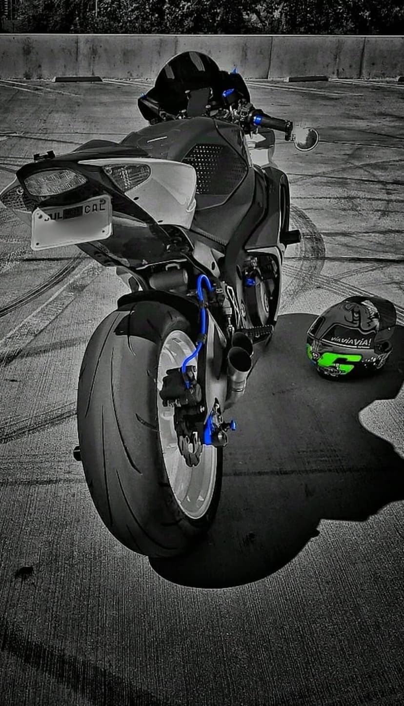 Black sportbike motorcycle with blue accents and a green racing helmet parked on an asphalt street with trees.