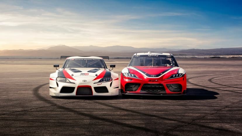 Two Toyota Supra race cars side-by-side on a desert track under a sunset sky with mountains in the background.