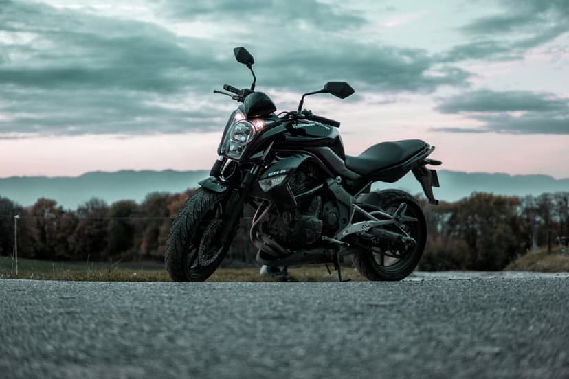 Matte black motorcycle parked on asphalt under a dramatic orange sunset sky with silhouettes of distant hills.
