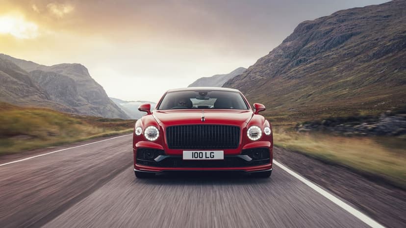 Red luxury sedan driving on a mountain road between steep hills under a golden sunset sky with motion blur.