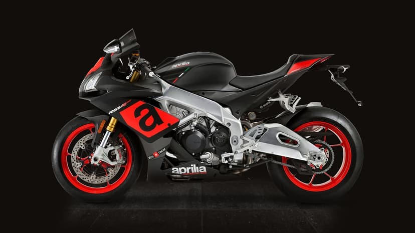 Profile of a matte black Aprilia RSV4 RR motorcycle with red wheels and silver frame in a dark studio setting.