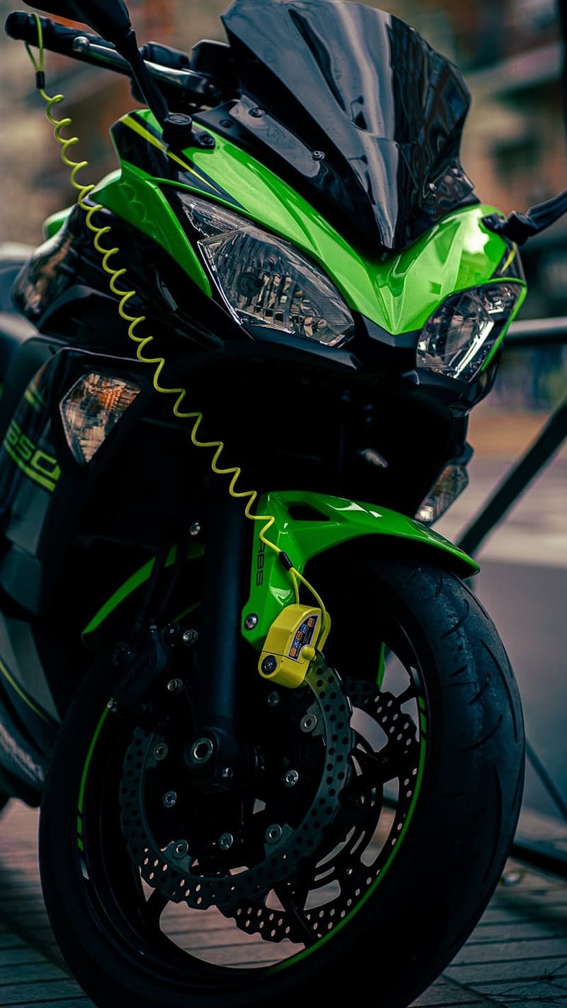Green Kawasaki motorcycle with a yellow disc lock on the front brake wheel, viewed from a low-angle perspective.