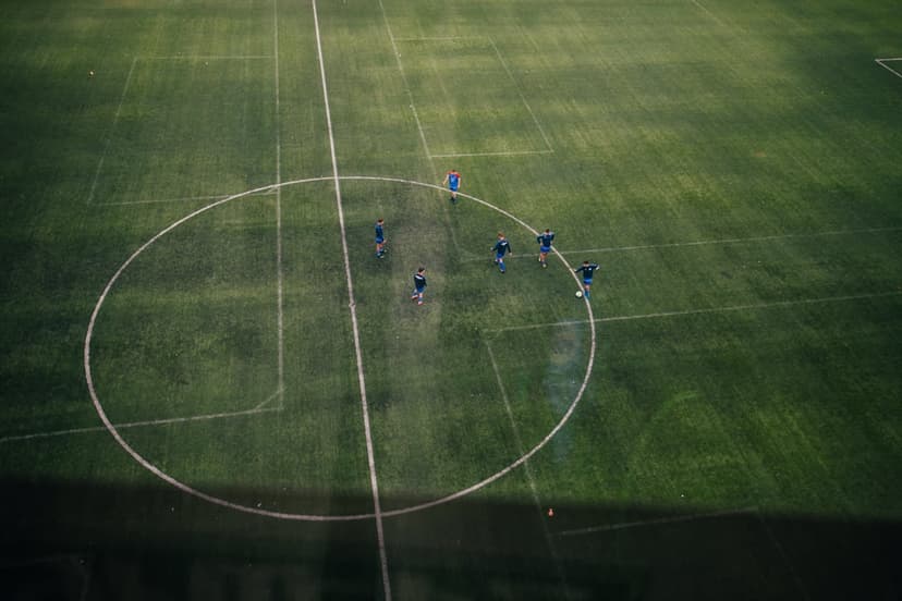 Soccer players move across a vibrant green grass pitch near a white center circle line during a live match.