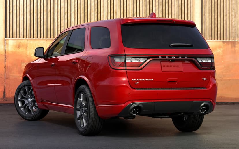 Red Dodge Durango RT SUV rear view parked by a corrugated metal wall with dual exhausts and dark alloy wheels.