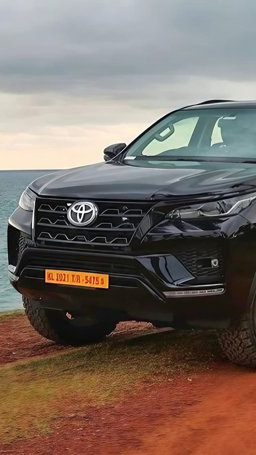 Black Toyota Fortuner parked on a rocky cliff edge with white crashing waves and dark clouds in the background.
