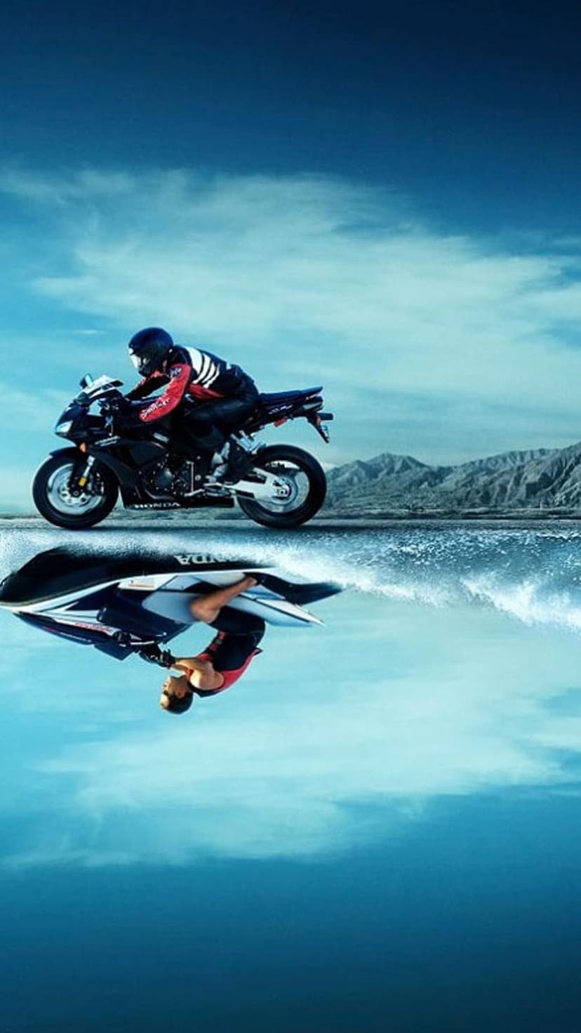 Motorcycle rider racing on a cliff above a mirrored reflection of a surfer in blue water under a clear sky.