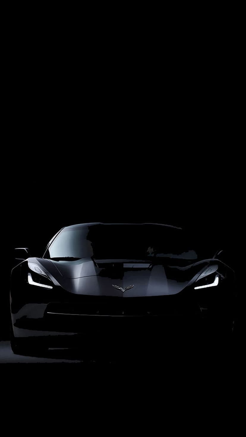 Black Corvette front view with illuminated LED headlights appearing from a dark, high-contrast background.