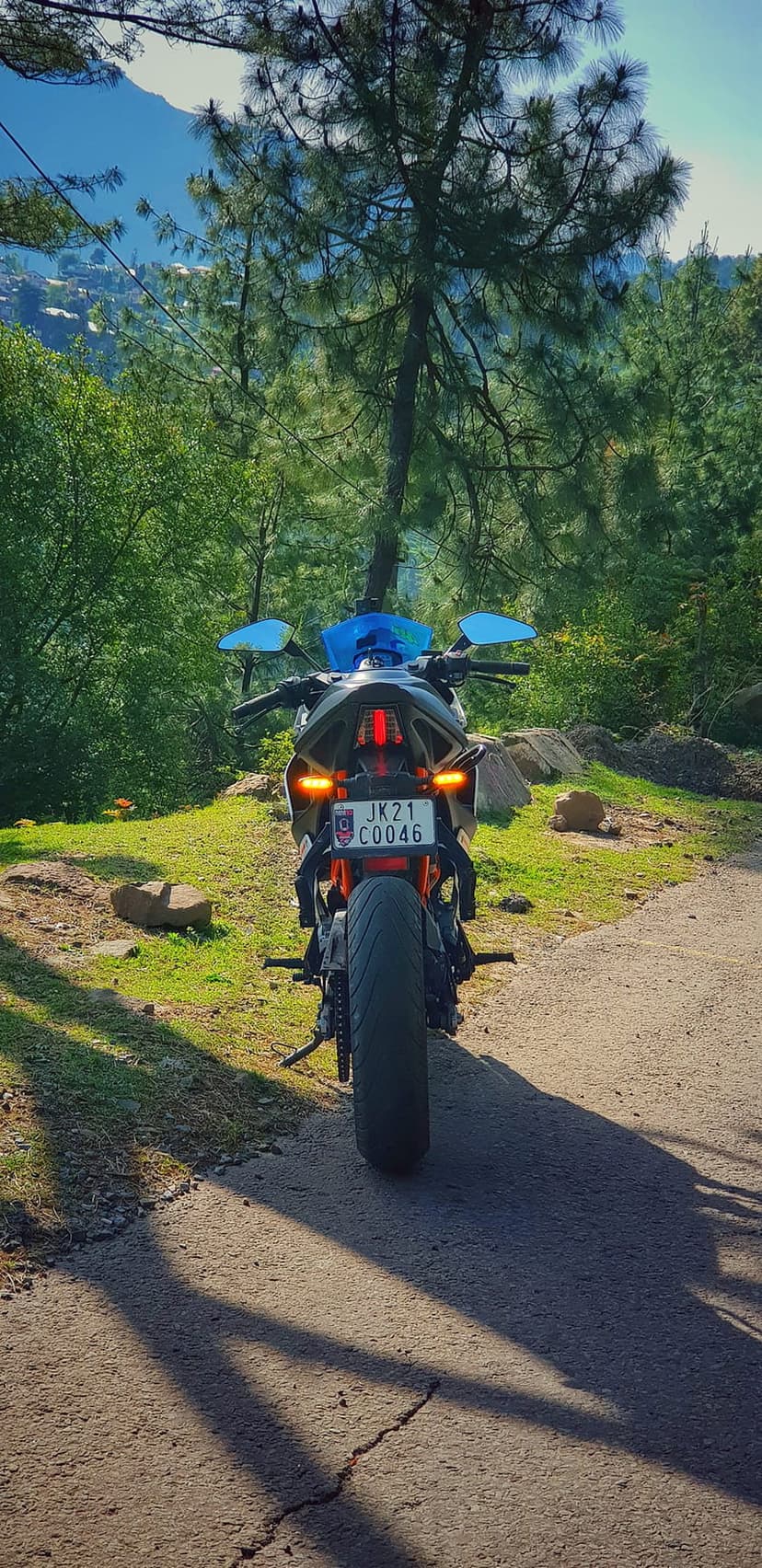 Sporty orange motorcycle parked on a paved mountain road surrounded by green trees under a clear blue sky.