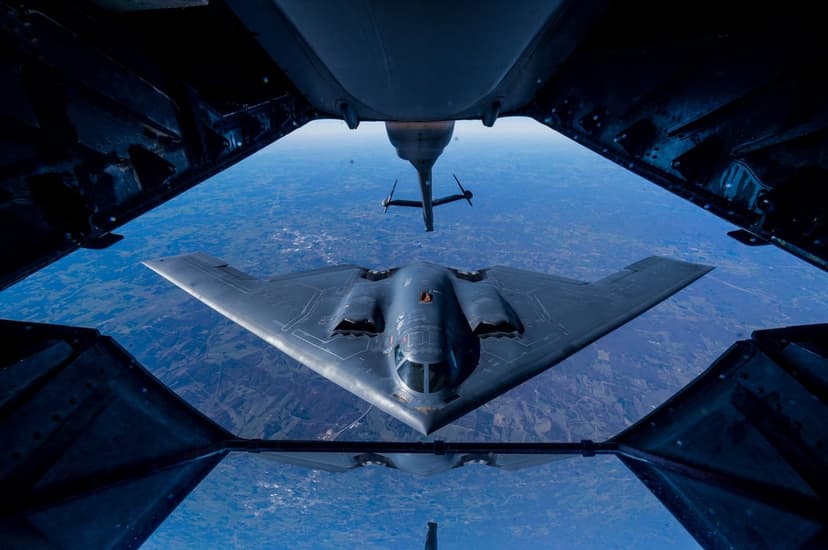 B-2 Spirit stealth bomber receiving fuel from a tanker aircraft boom over a layer of soft white clouds.