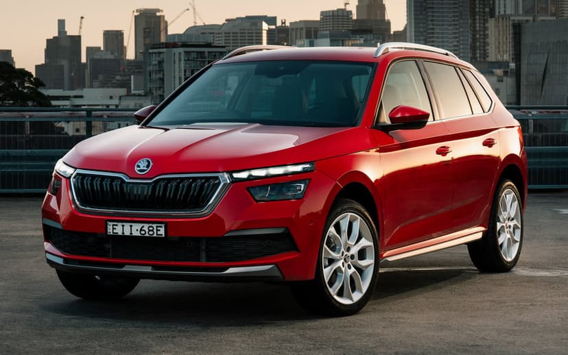 Red Skoda SUV on a rooftop with a blurred city skyline background under warm sunset lighting.
