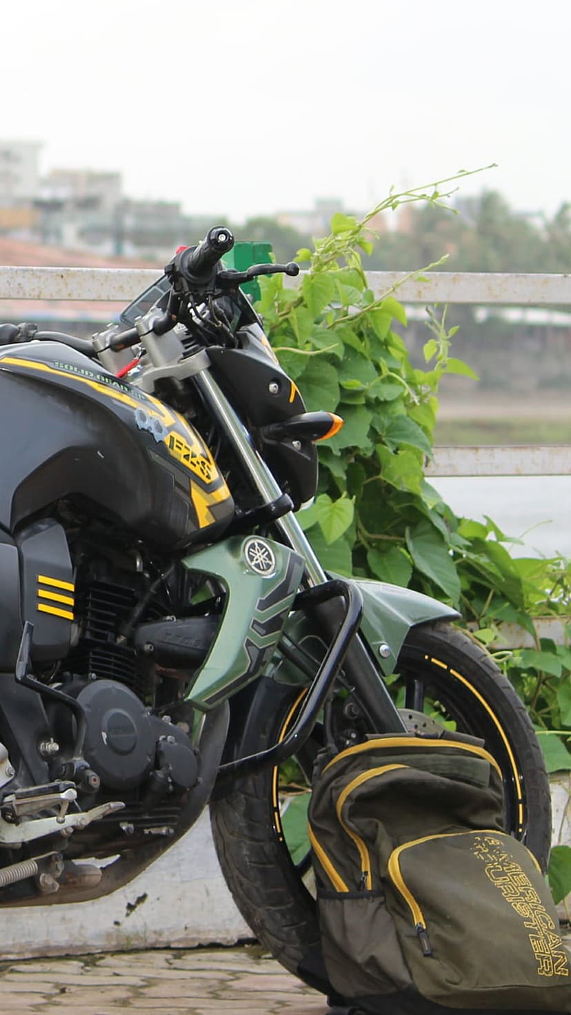 Black Yamaha motorcycle with green accents and a tactical backpack parked in front of thick garden foliage.