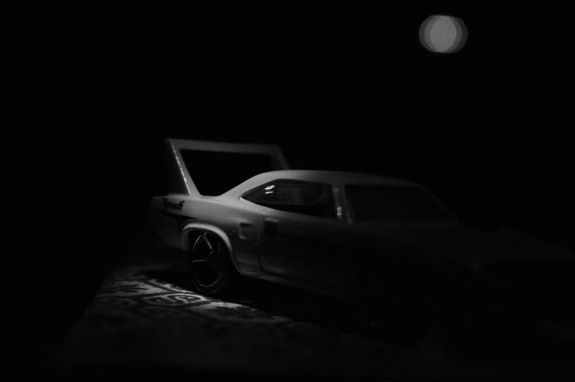 Classic muscle car with a high rear wing silhouetted against a dark, moonlit sky in a monochrome photograph.