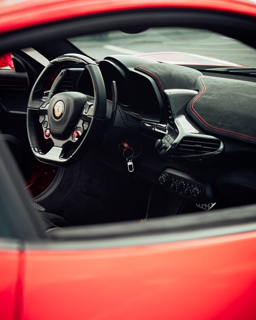 Ferrari steering wheel with yellow horse emblem and red leather accents in a luxury car interior cockpit.