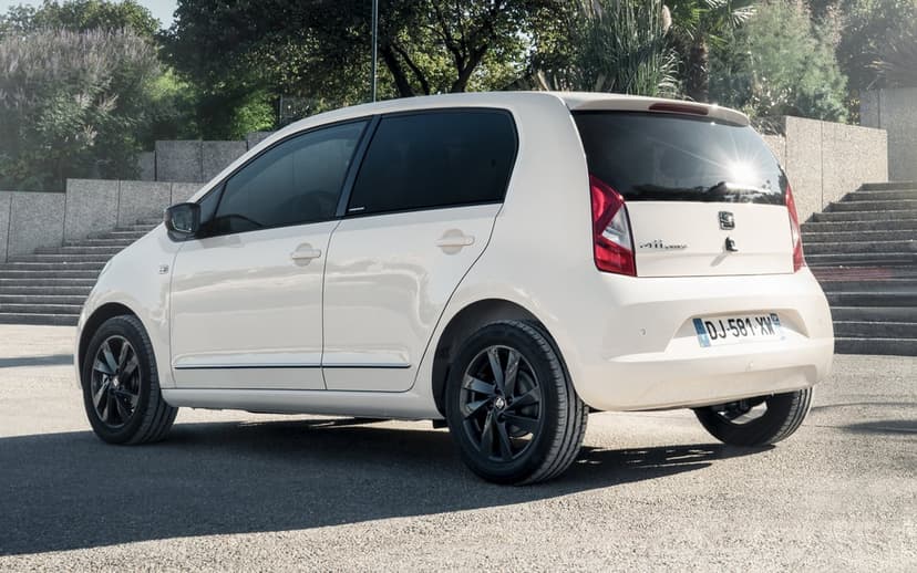 Rear view of a white SEAT Mii hatchback with black rims parked near stone stairs in bright sunlight.