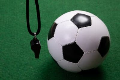 Soccer ball and referee's whistle on green surface