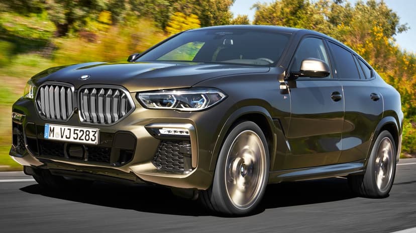 A dark bronze BMW X6 SUV driving on a road with motion blurred wheels and a sunlit autumn forest background.