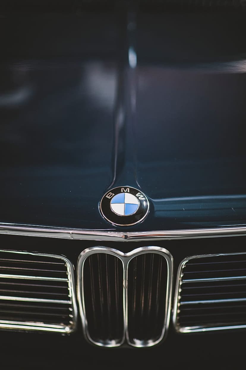 BMW roundel emblem and chrome kidney grille on a dark blue vintage car hood shown in a detailed low-angle shot.