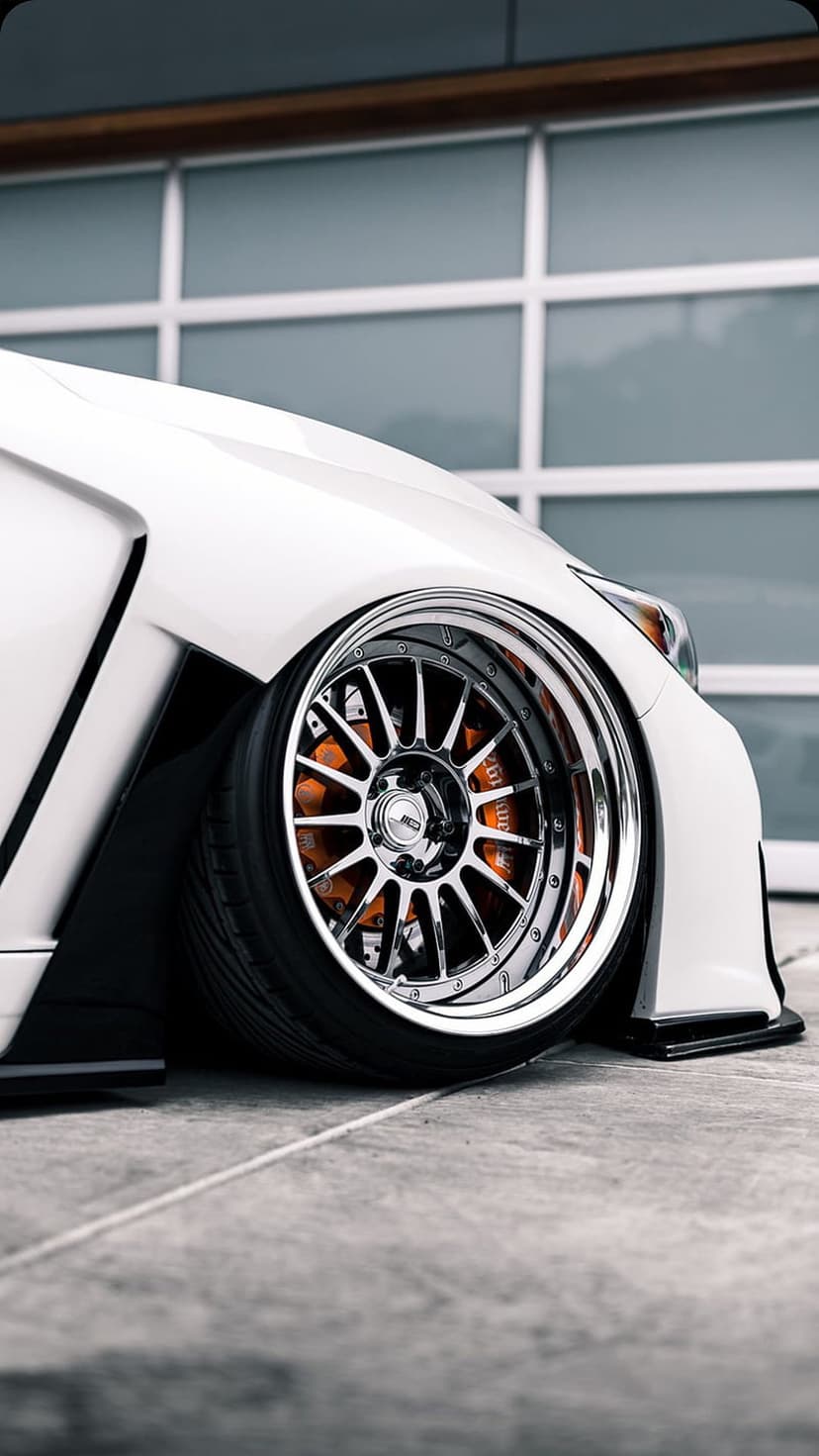 Orange brake calipers visible through a multi-spoke chrome wheel on a white sports car in a modern garage.