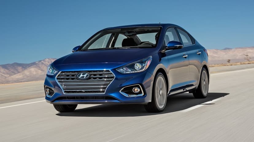 Dark blue sedan driving on a desert highway under a clear sky with distant mountains and visible motion blur.
