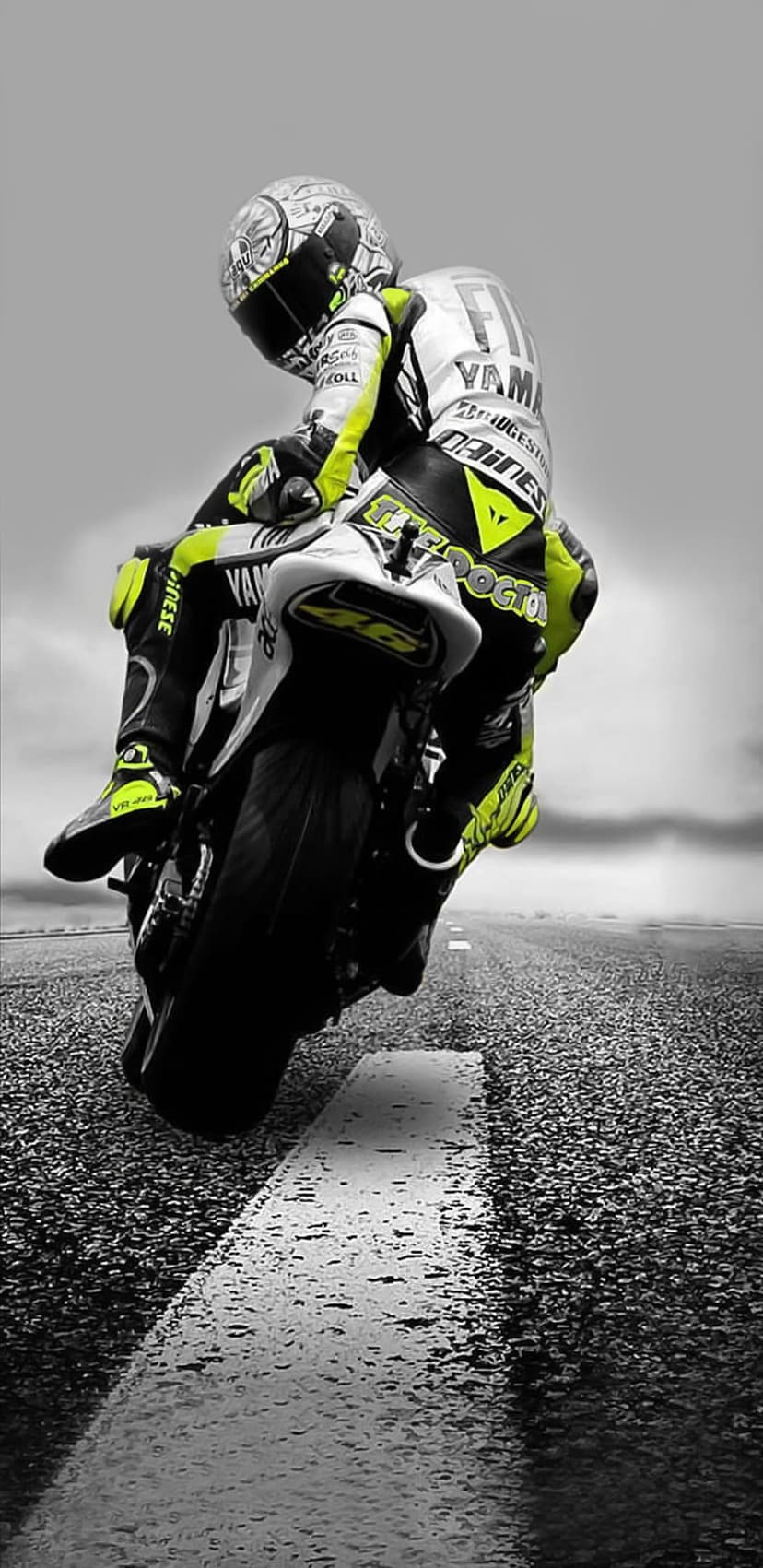 Valentino Rossi leans a Yamaha motorcycle into a racetrack corner in a monochrome shot with yellow suit details.