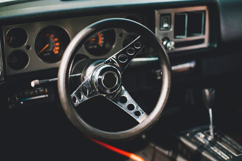 Classic car steering wheel and dashboard with glowing orange analog gauges and chrome details in low light.