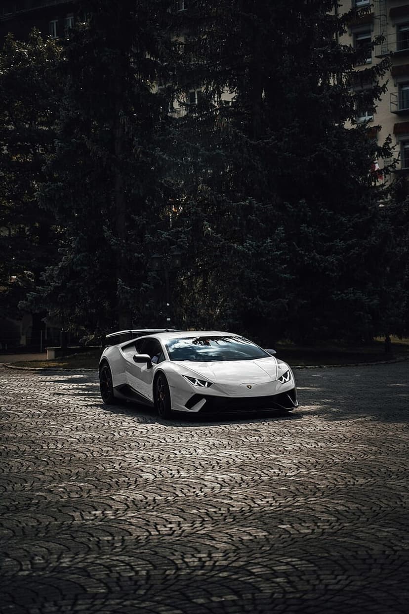 White Lamborghini Huracan parked on a textured cobblestone street under dramatic night lighting in the city.