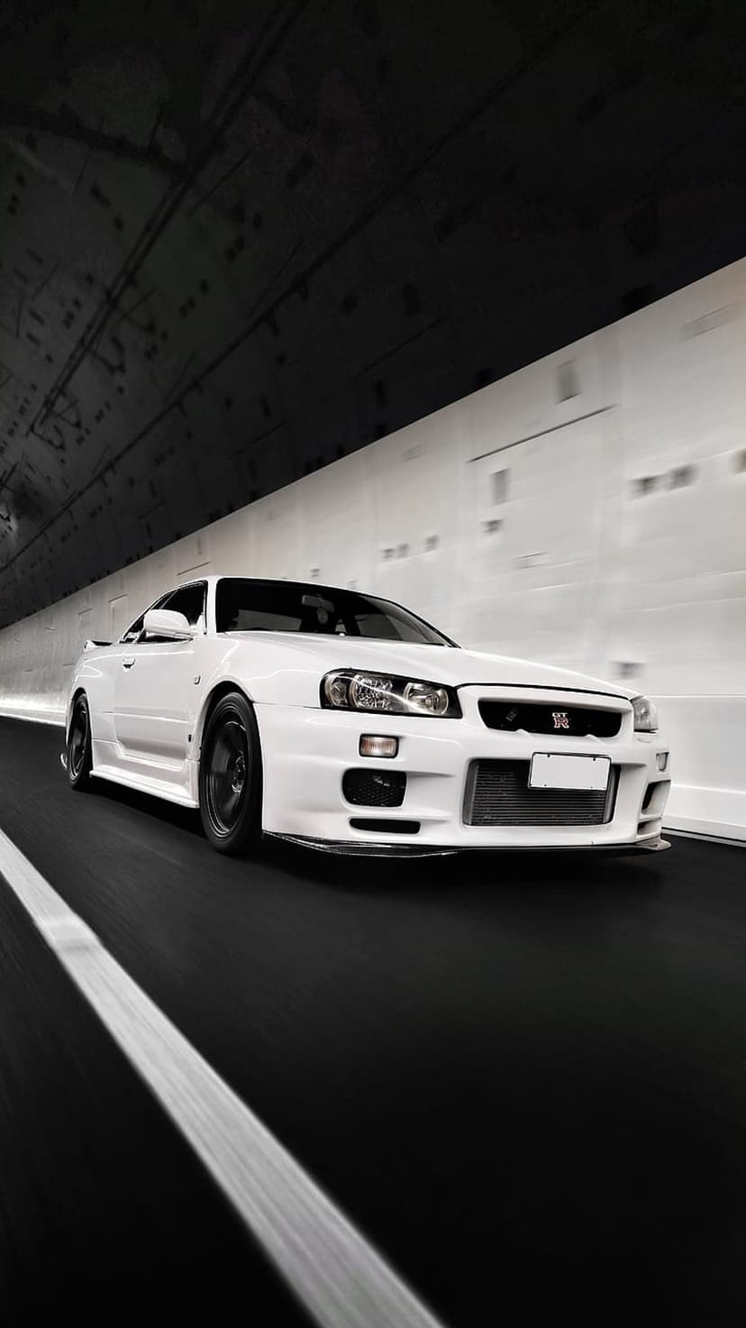 White Nissan Skyline R34 GT-R sports car speeds through a brightly lit tunnel with visible motion blur.