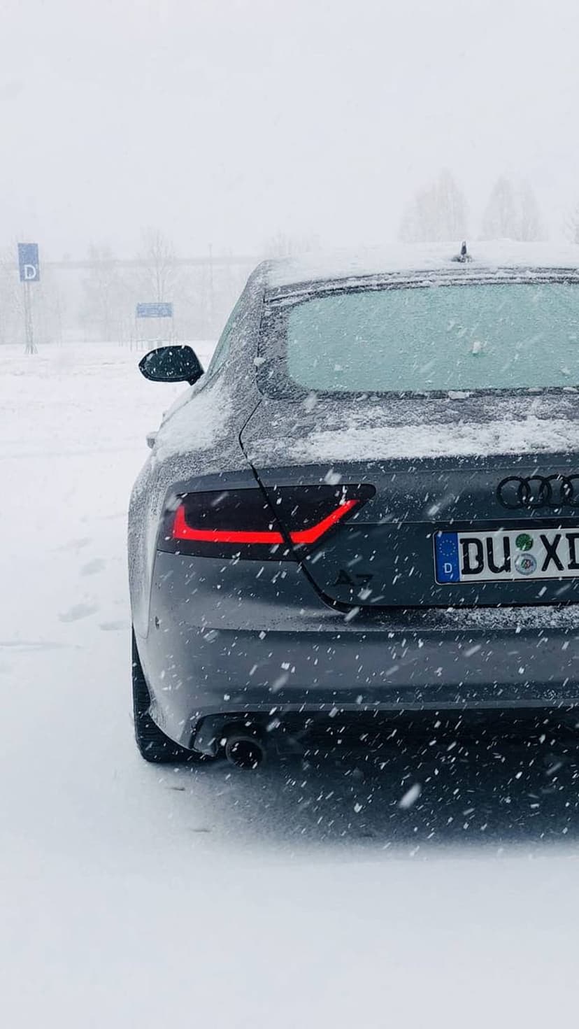 Audi A7 rear exterior with glowing red LED tail lights parked in a heavy snowfall during a winter storm.