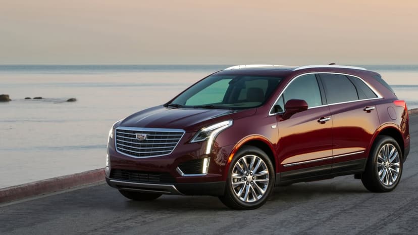 Deep red Cadillac XT5 luxury SUV parked on a coastal road during golden hour with a calm ocean background.
