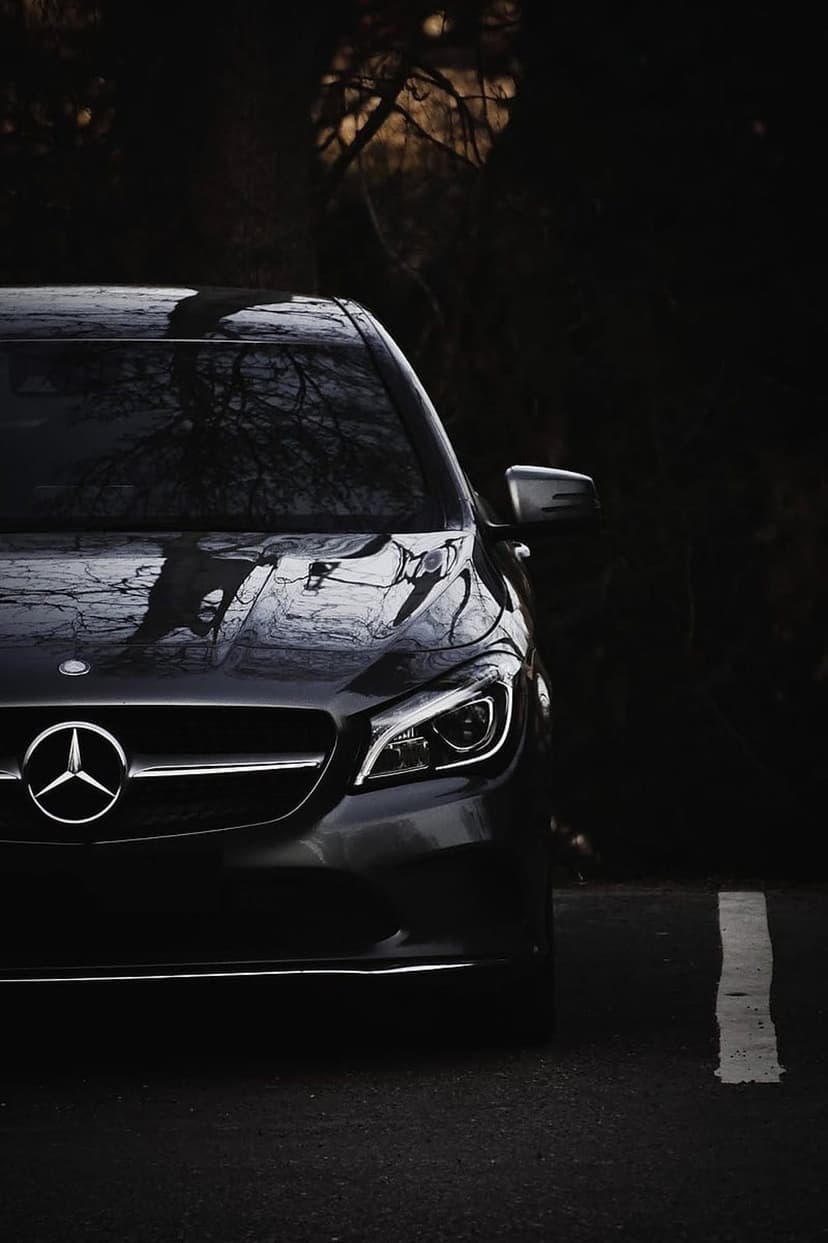 Mercedes-Benz CLA luxury sedan with glowing LED headlights and a silver star emblem on dark asphalt.