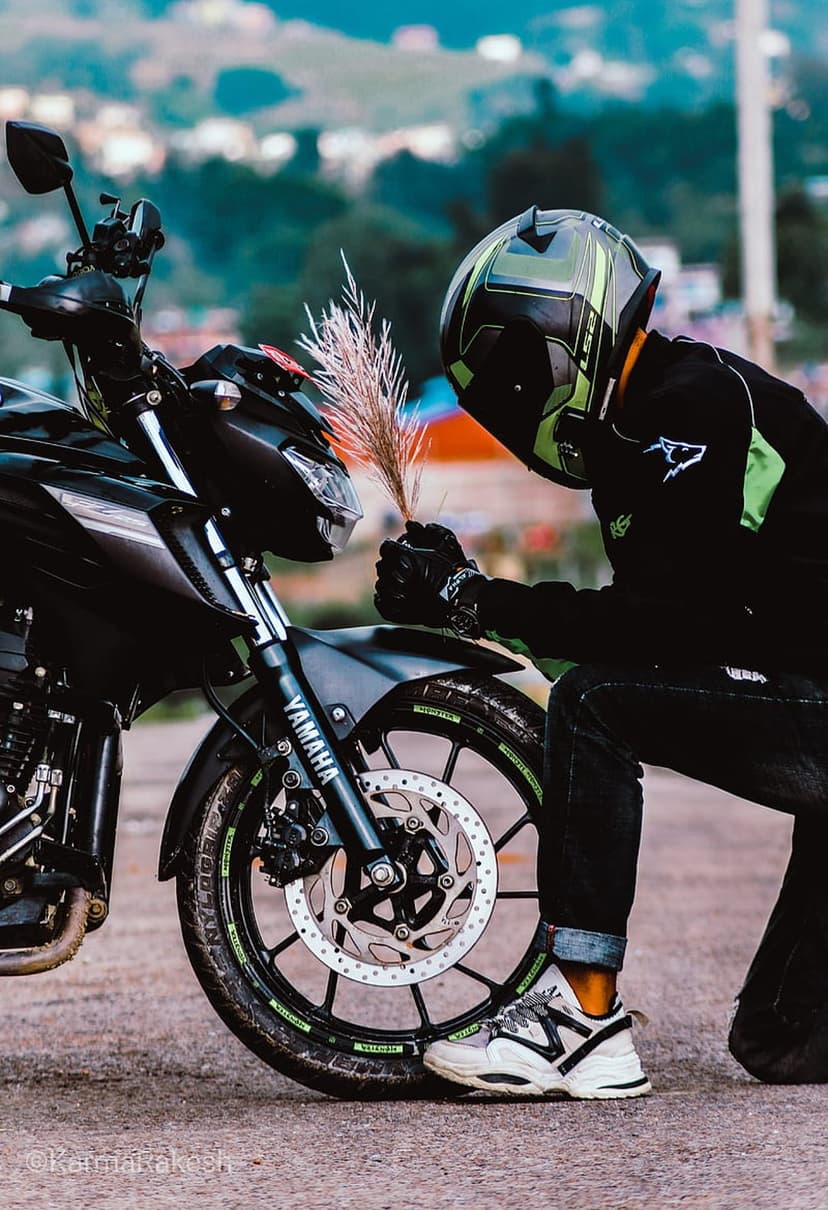 Biker in a green helmet kneels by a black Yamaha motorcycle while holding a plume of dried pampas grass.