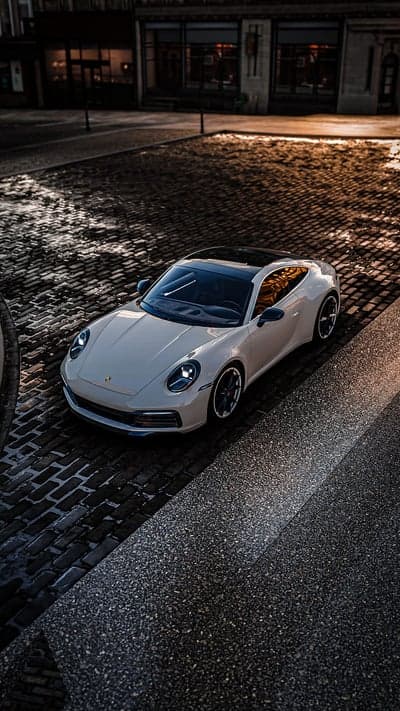 White Porsche 911 on Wet Cobblestone Street at Dusk