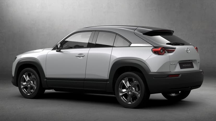 White Mazda MX-30 SUV viewed from the rear corner against a minimalist gray textured wall in soft studio light.