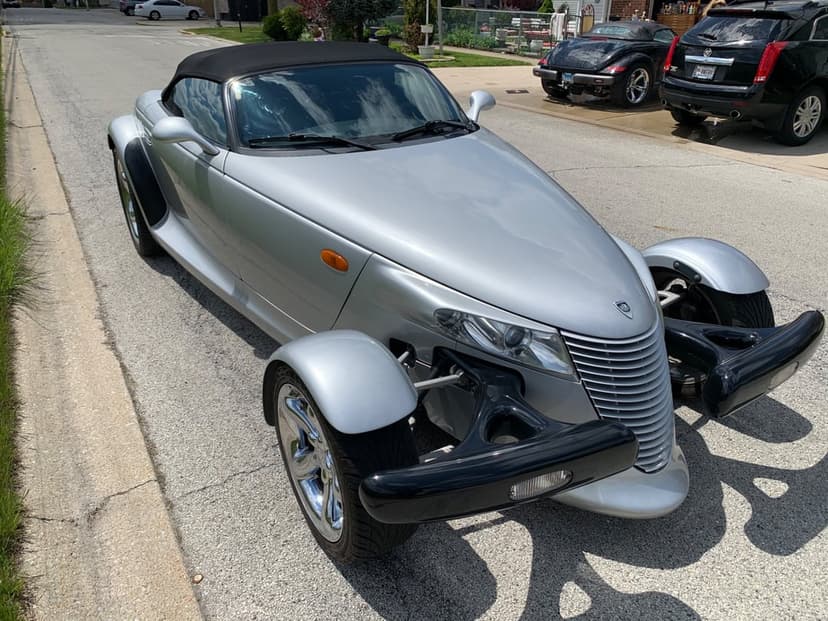 Silver Plymouth Prowler convertible with open-wheel fenders parked on a suburban street in bright daylight.