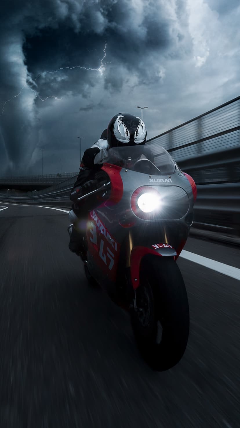 Suzuki sportbike rider speeds through a lightning-filled thunderstorm on a dark, wet, winding road.