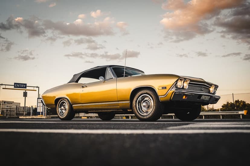 Gold 1968 Chevrolet Chevelle SS convertible on asphalt under a cloudy sunset sky with warm evening light.