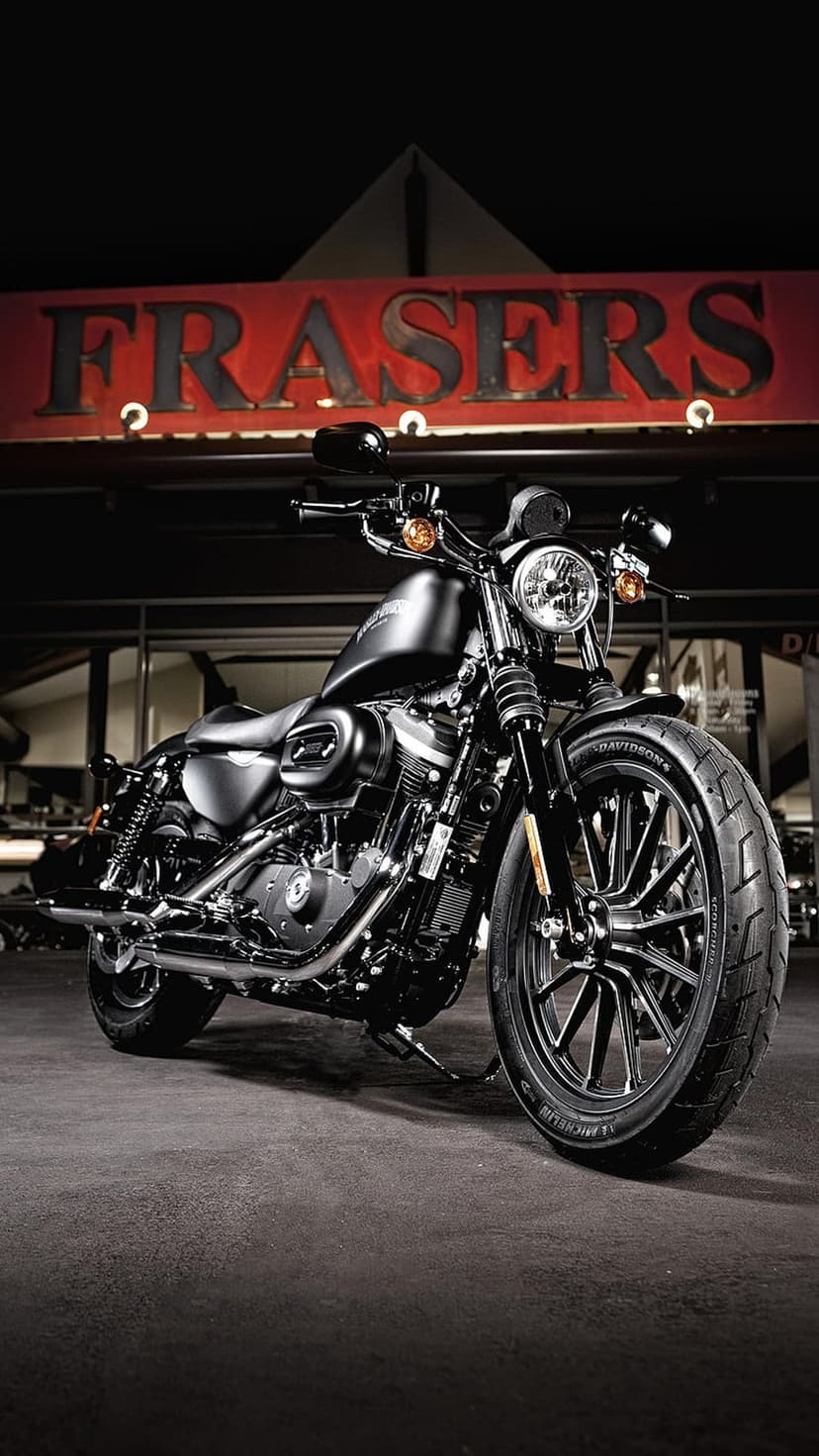 Black Harley Davidson motorcycle with chrome engine parked beneath a glowing red neon Frasers sign at night.