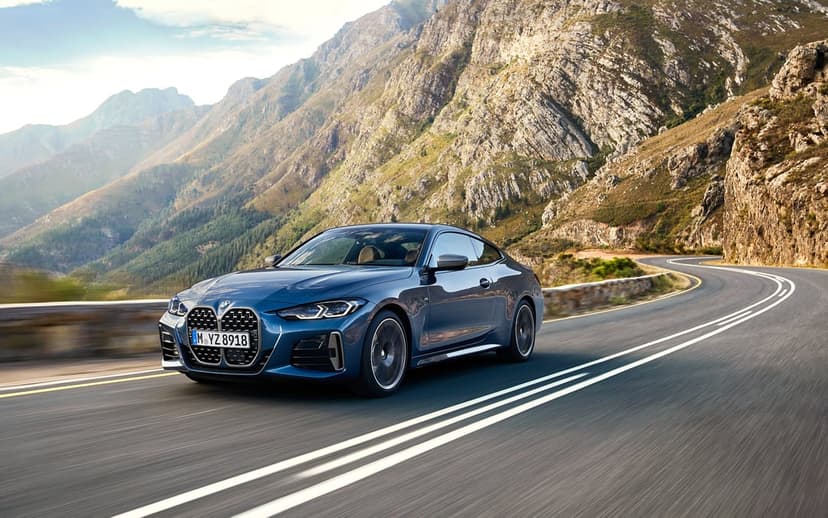 Blue BMW 4 Series Coupe driving fast on a winding mountain road with rugged cliffs and motion-blurred asphalt.
