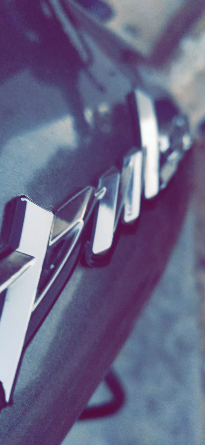 Chrome V8 emblem mounted on a dark textured vehicle surface with bright reflections on the metallic edges.