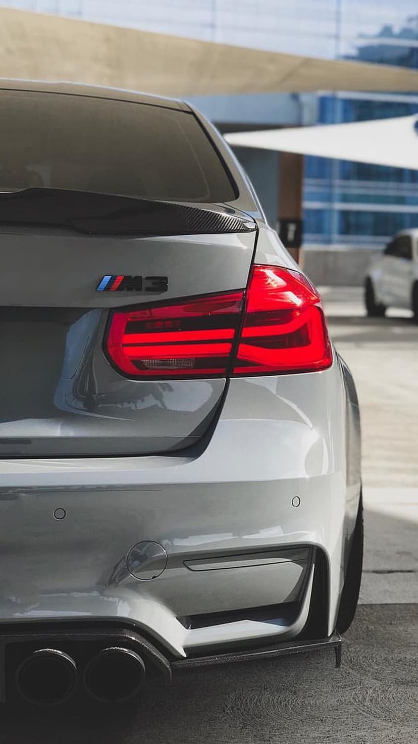 BMW M3 rear end showcasing red LED taillights, silver badging, and quad exhaust pipes on a grey metallic car body.